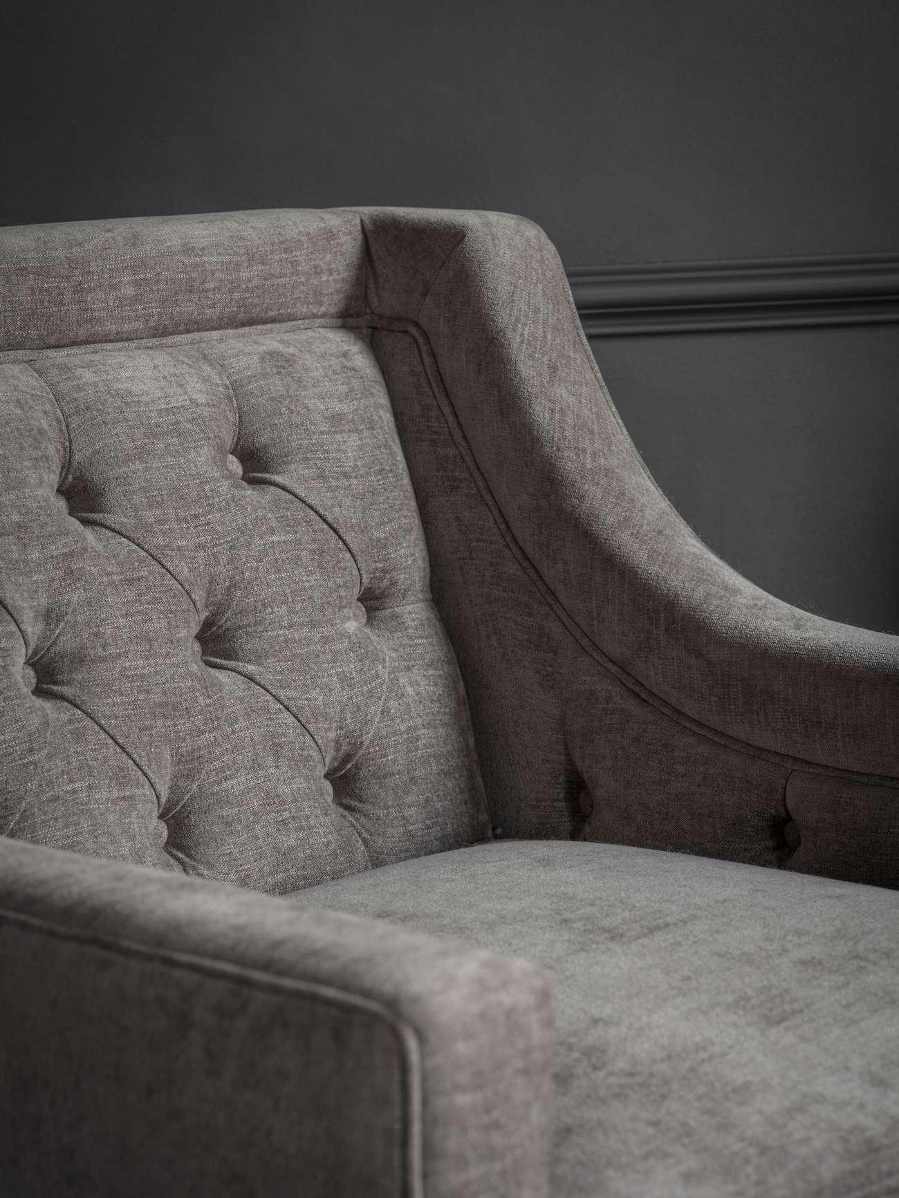 Warm grey armchair with buttoned backrest and curved arm detail.