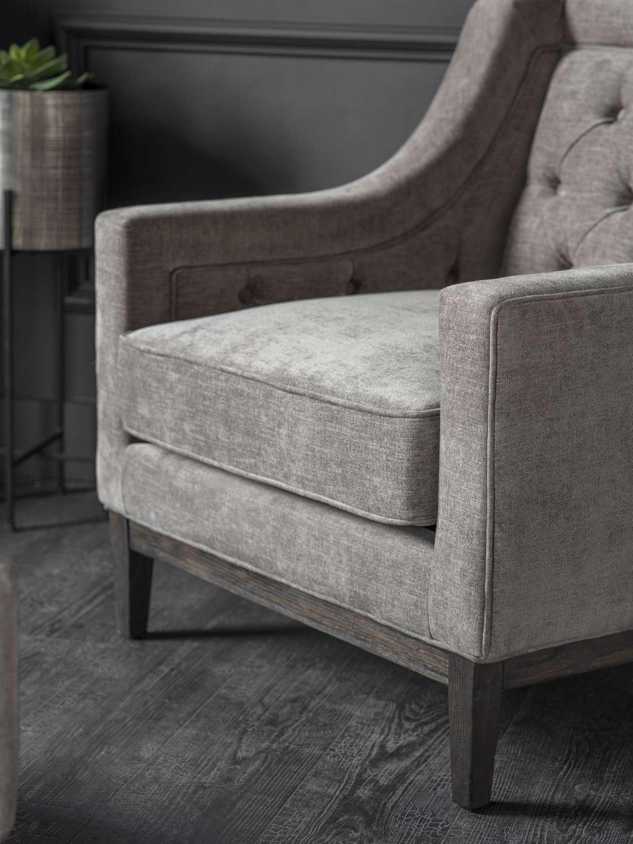 Warm grey armchair with buttoned backrest and dark wooden legs.