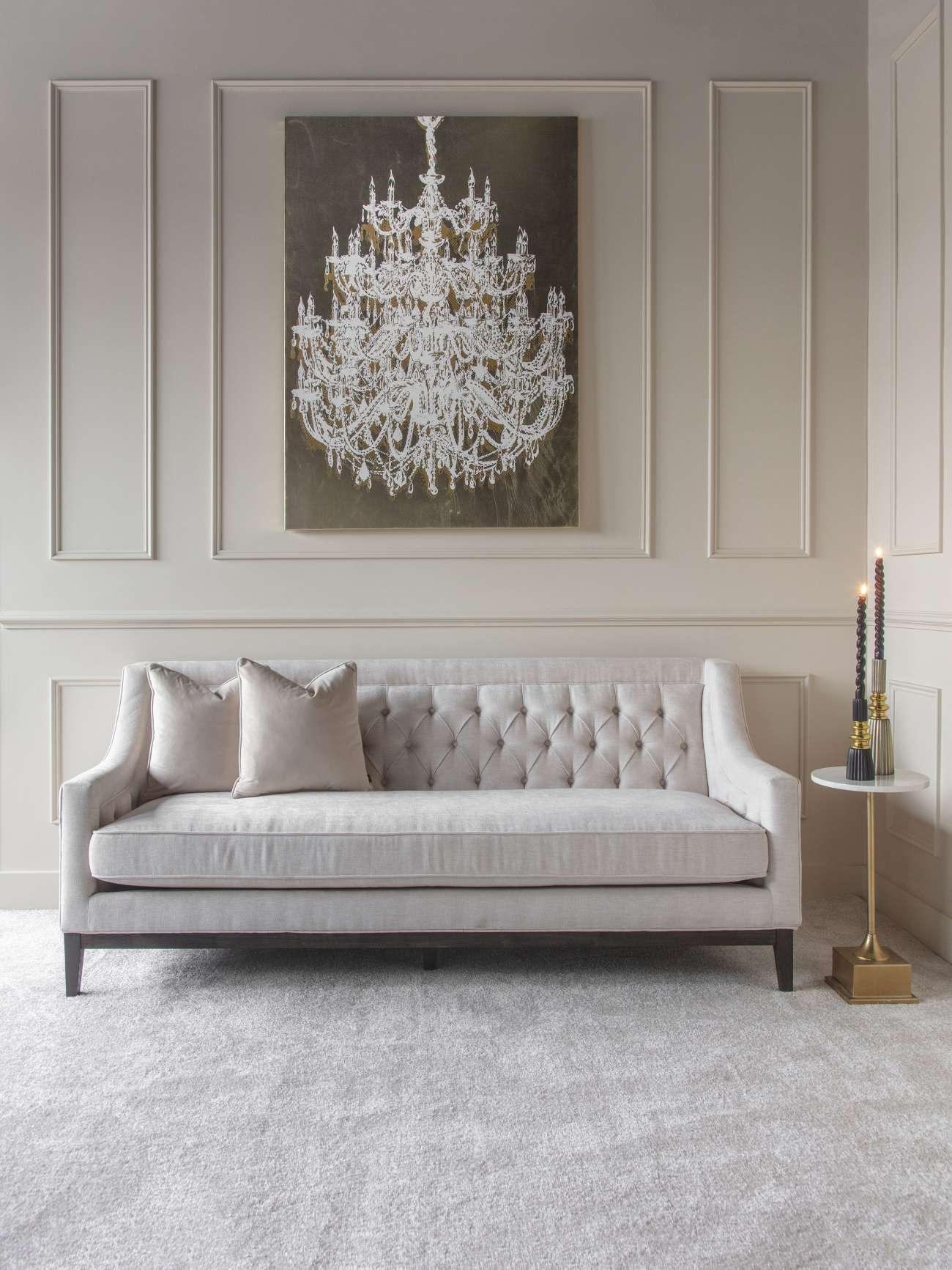 Ivory buttoned sofa in elegant room with chandelier artwork and side table.