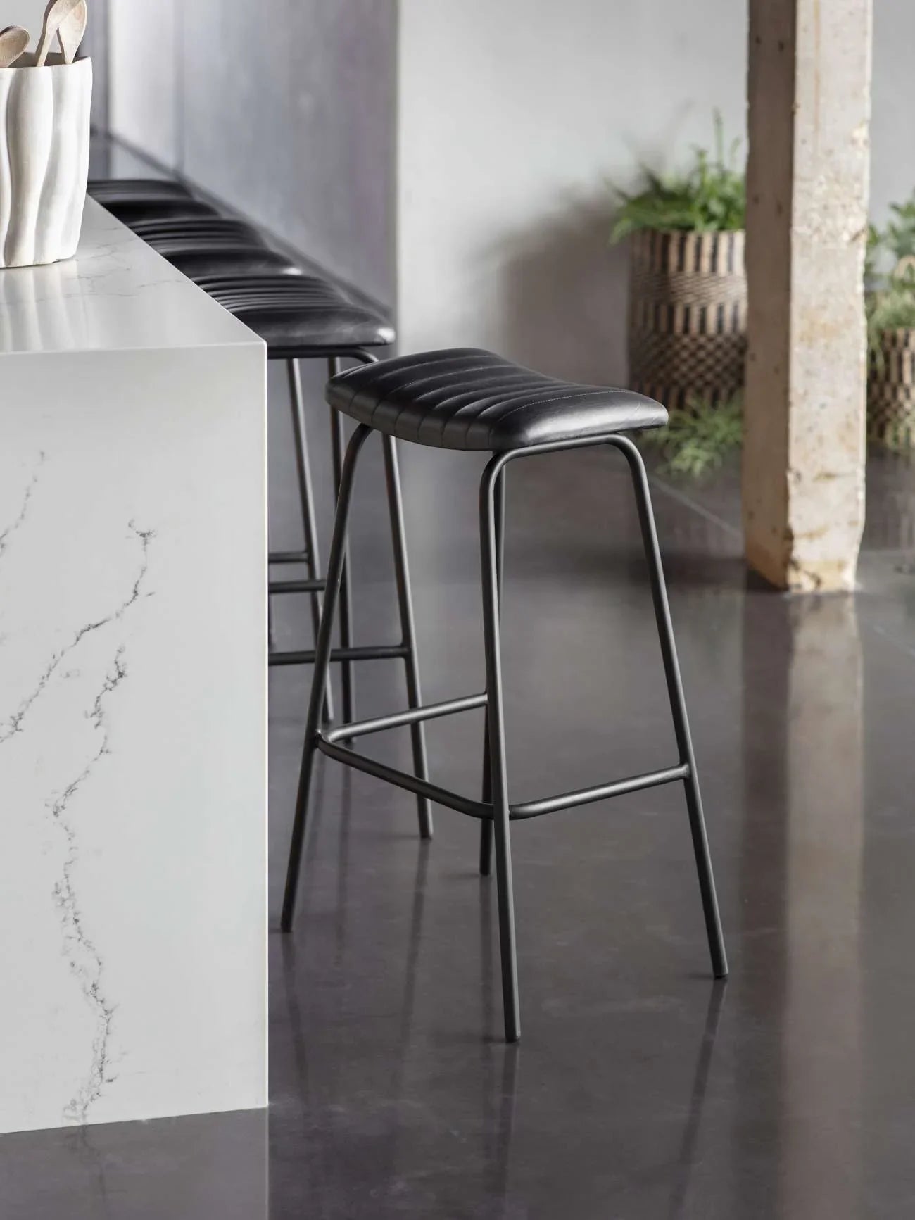 Charcoal leather bar stool beside a marble countertop in a modern kitchen.