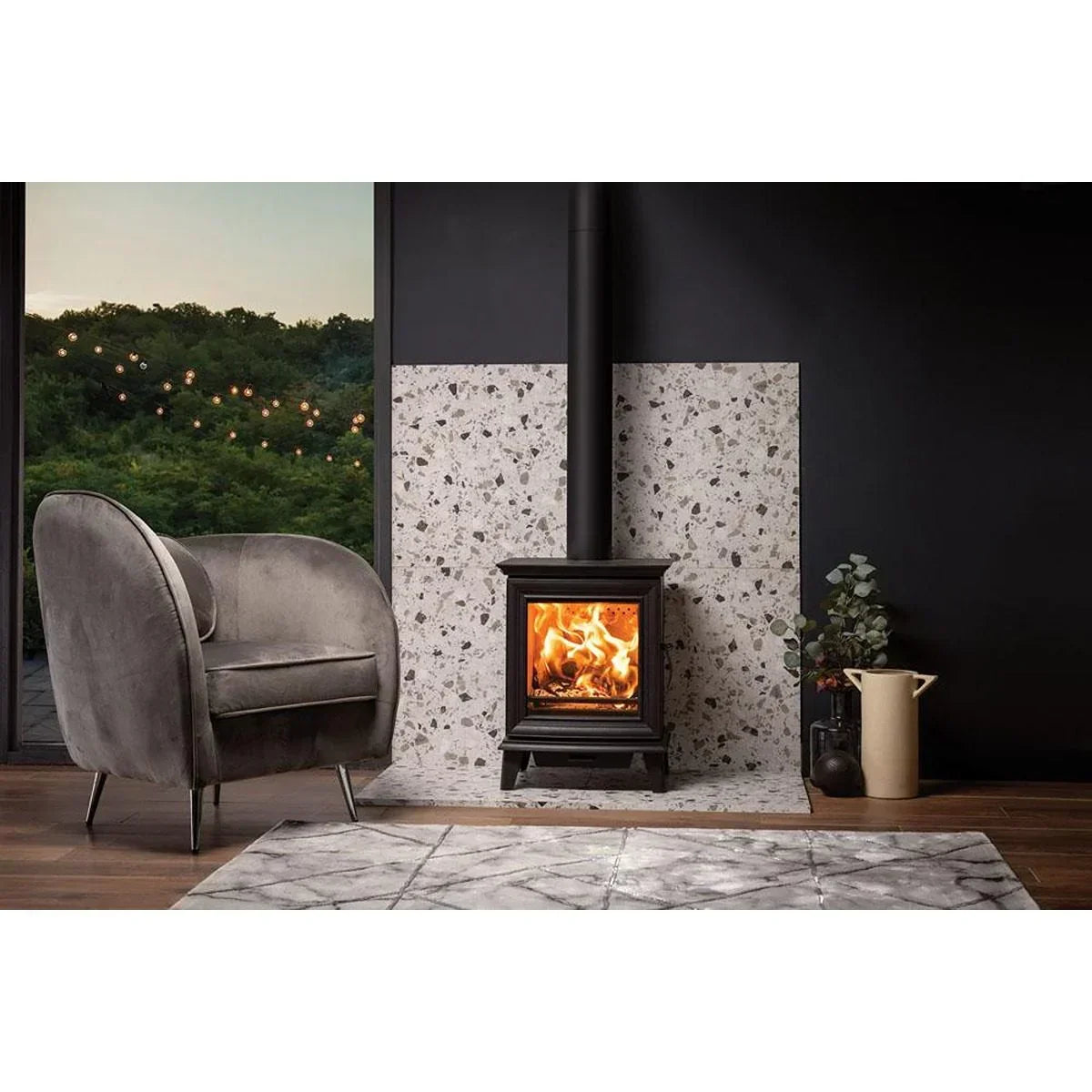 Grey fabric accent chair beside wood burning stove on stone hearth in modern living room