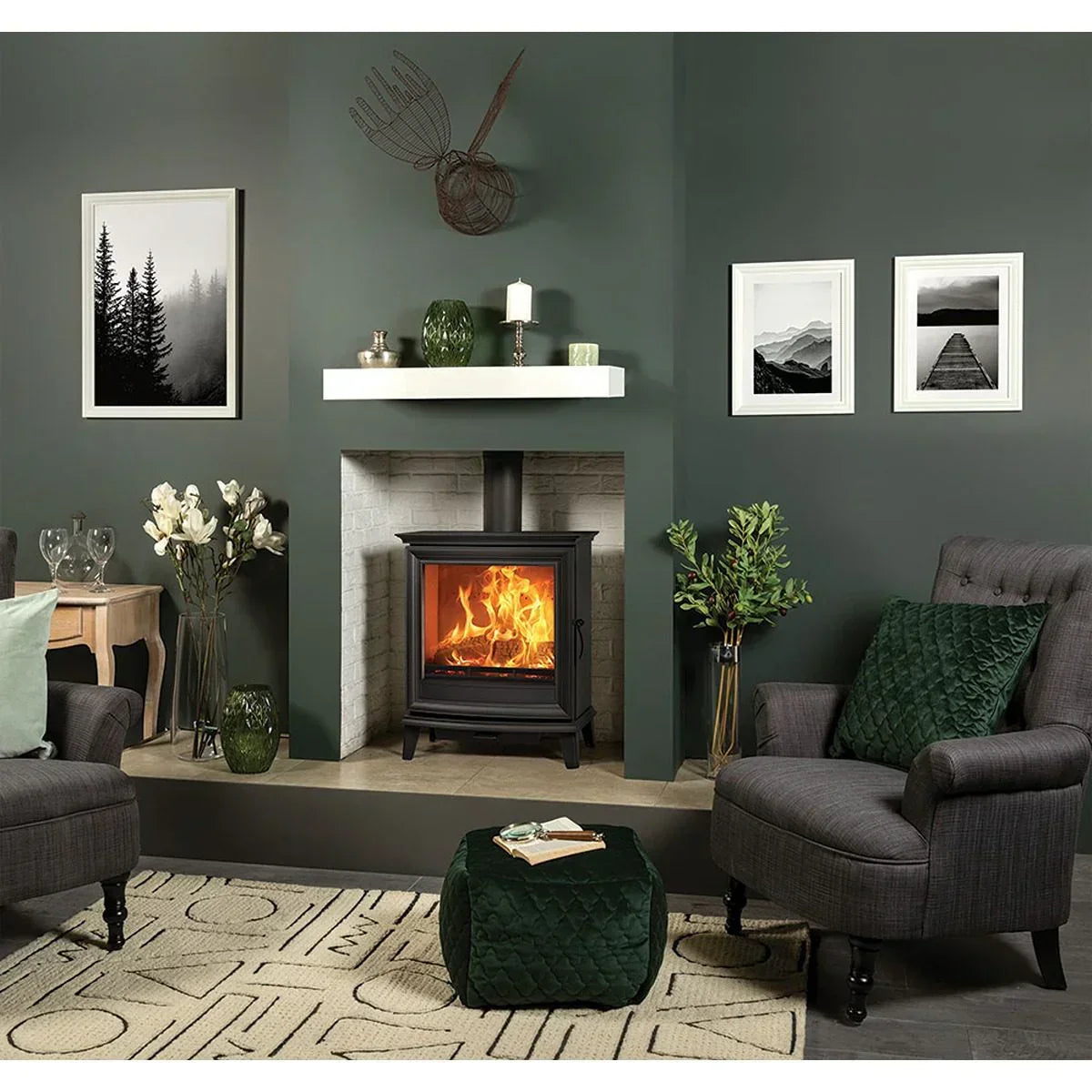 Grey armchair with green cushion and matching pouffe in modern living room by log burner fireplace