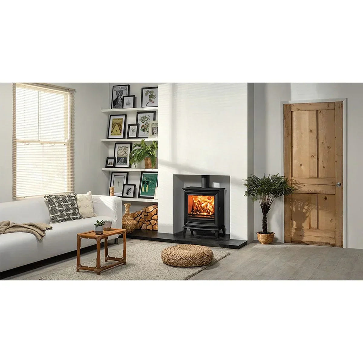 Living room with wood burning stove, white sofa, rug, and wall art on shelves