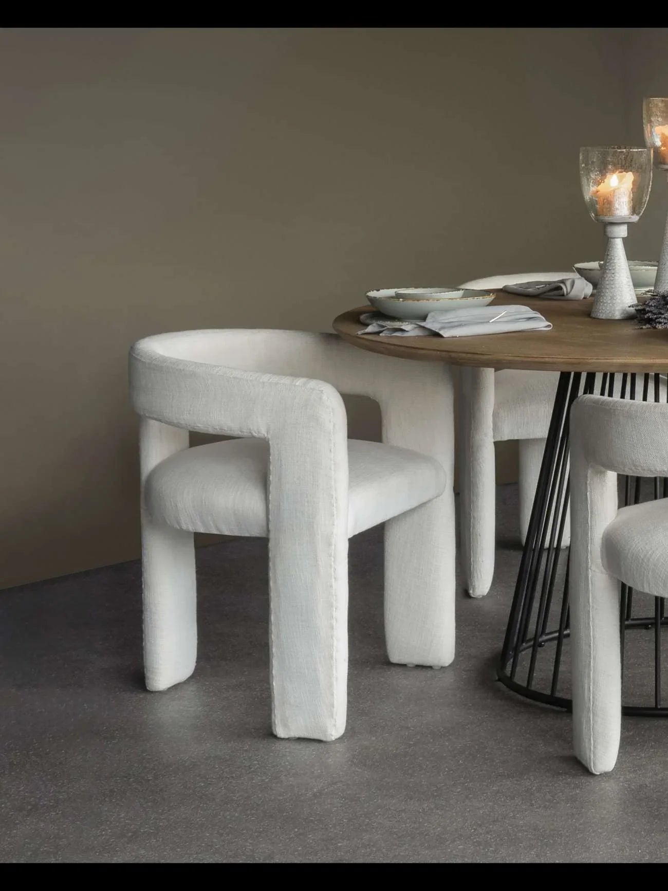 Ivory upholstered chair by a round table with candles and tableware.