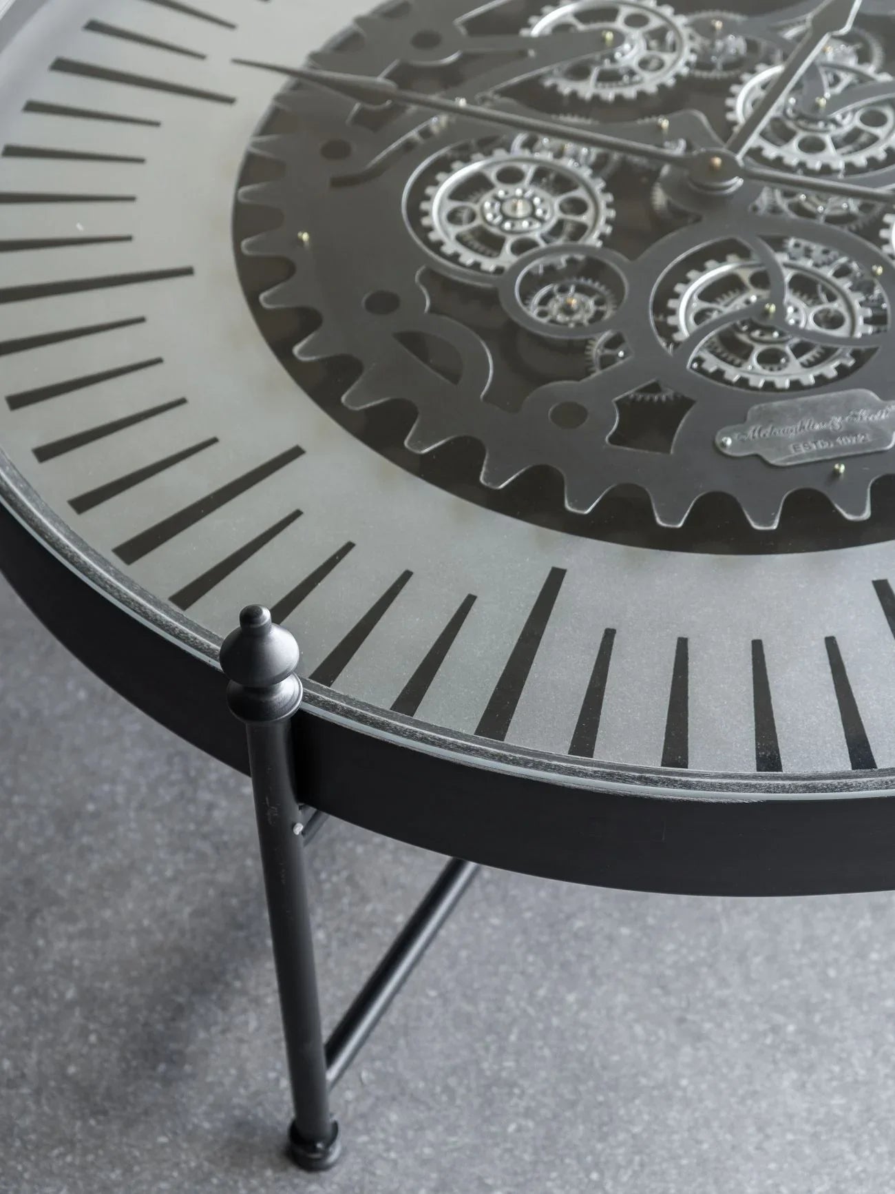 Black metal clock table with intricate moving gears and Roman numerals.