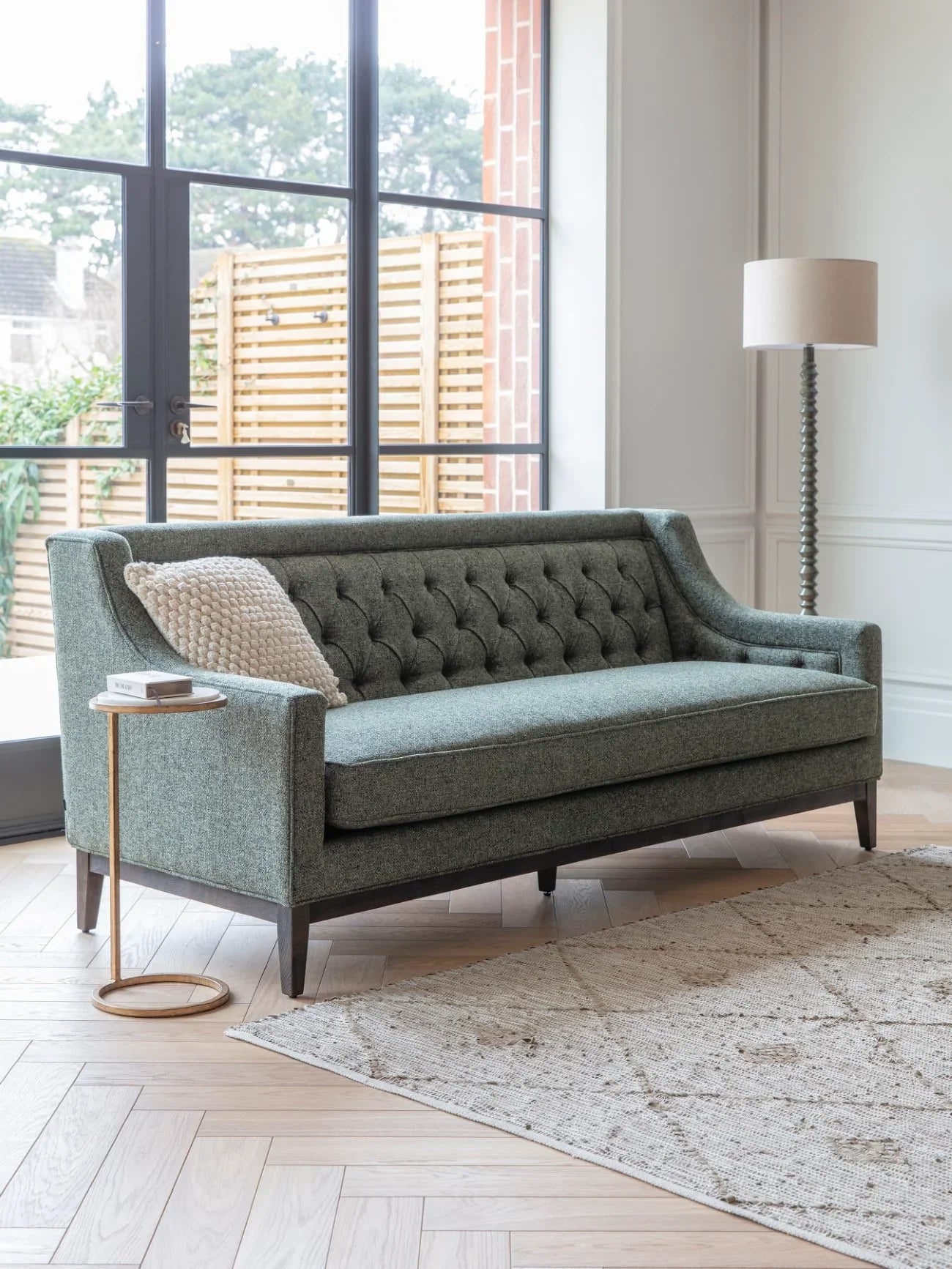 Forest green sofa in bright living room with lamp and side table.