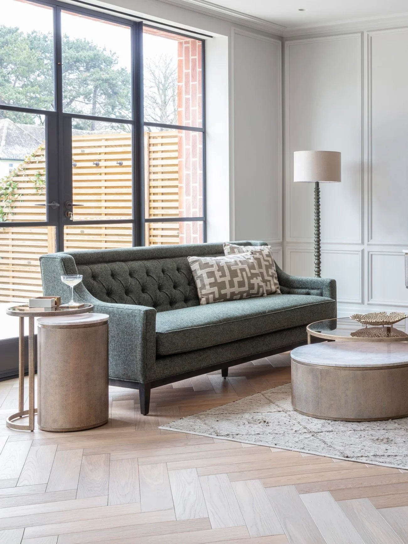 Forest green sofa in elegant living room with wooden tables and floor lamp.