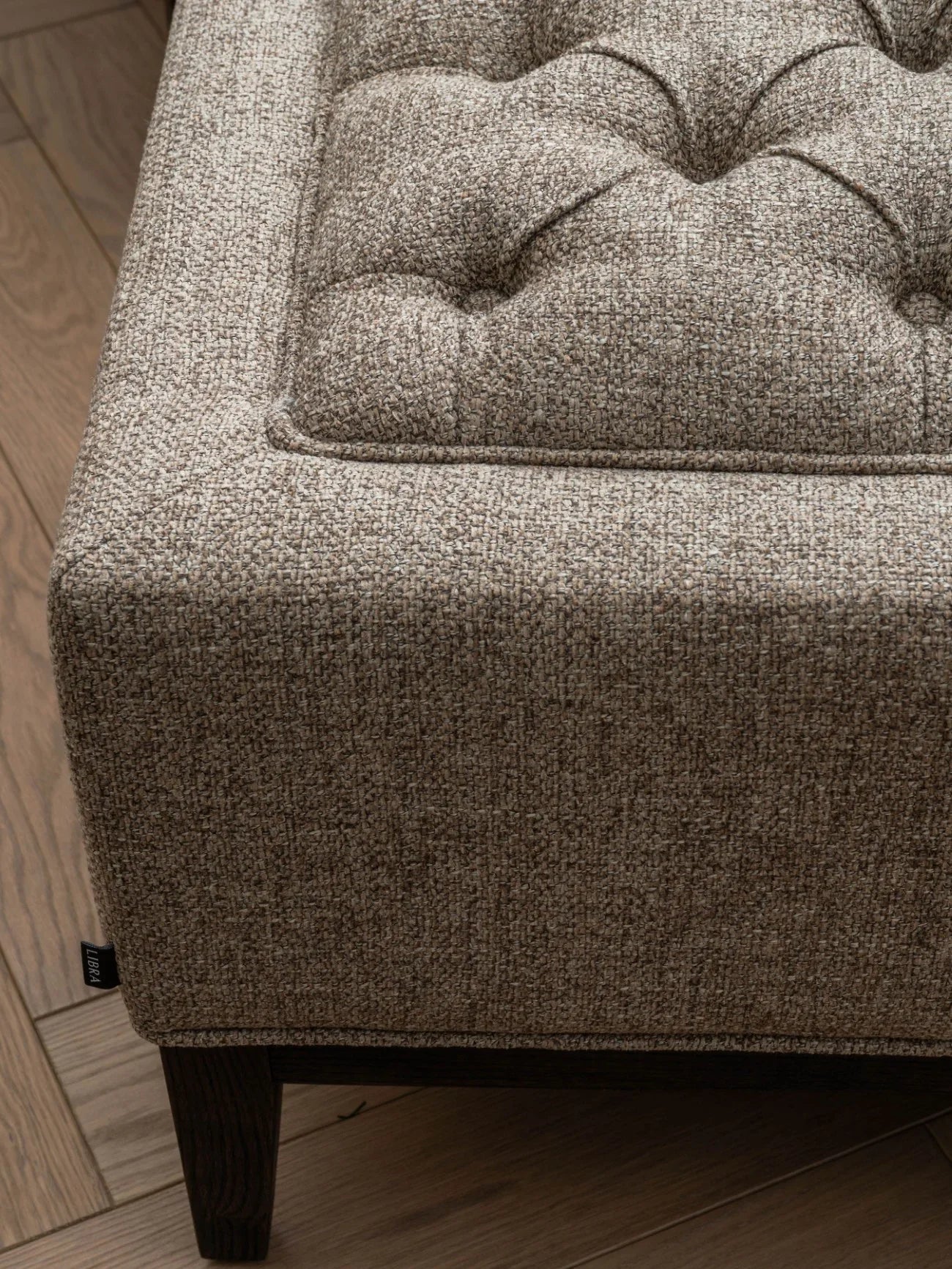 Dark taupe stool corner with buttoned texture and wooden leg detail.