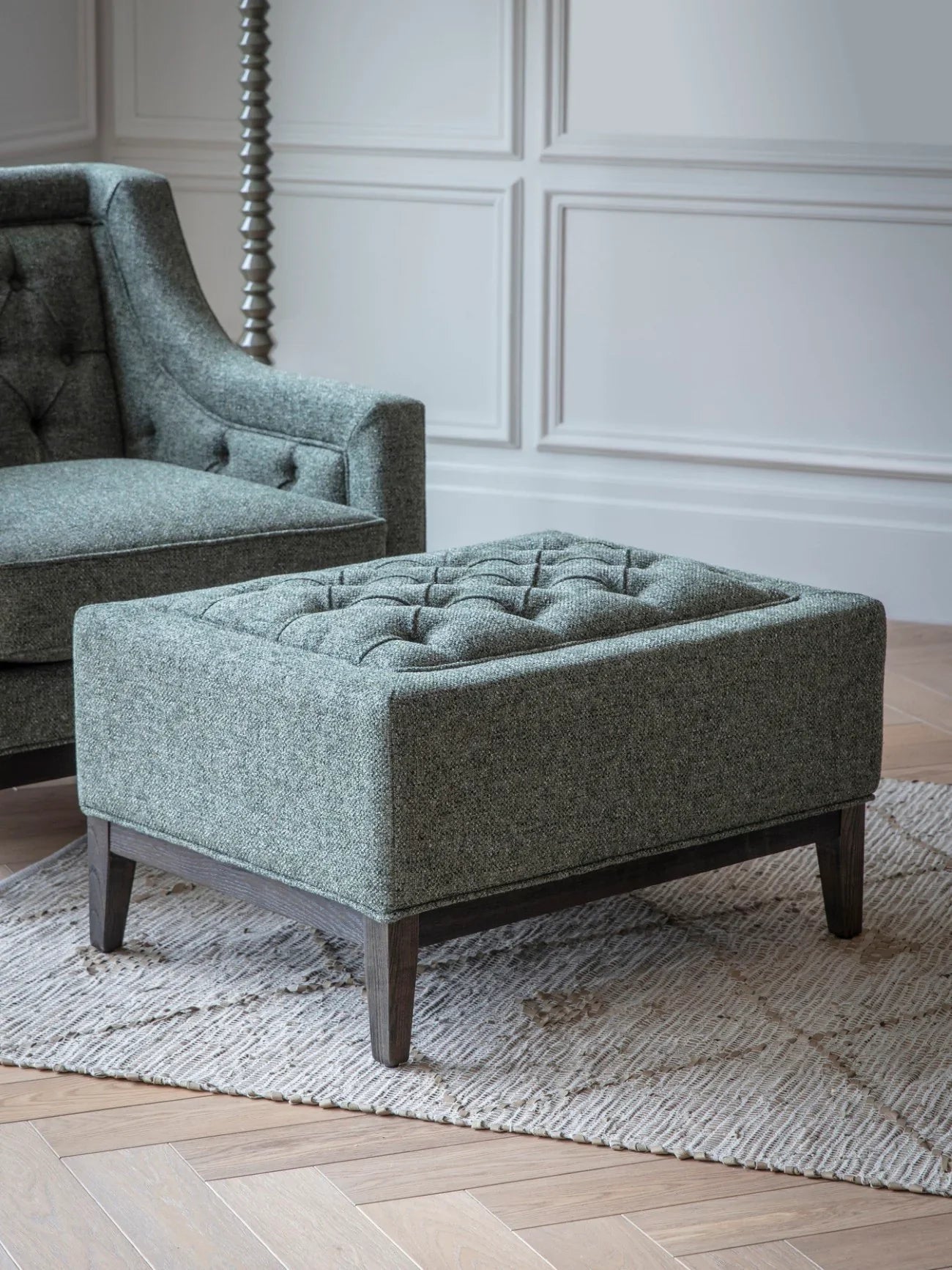 Forest green stool with buttoned top on a patterned rug.