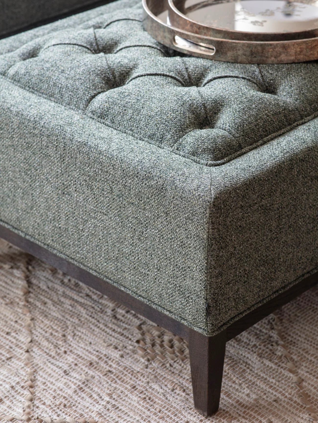 Forest green ottoman with buttoned texture and dark wooden legs.