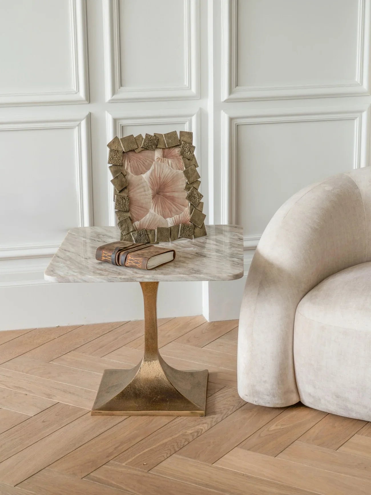 Marble side table with brass base beside a beige sofa and decorative frame.