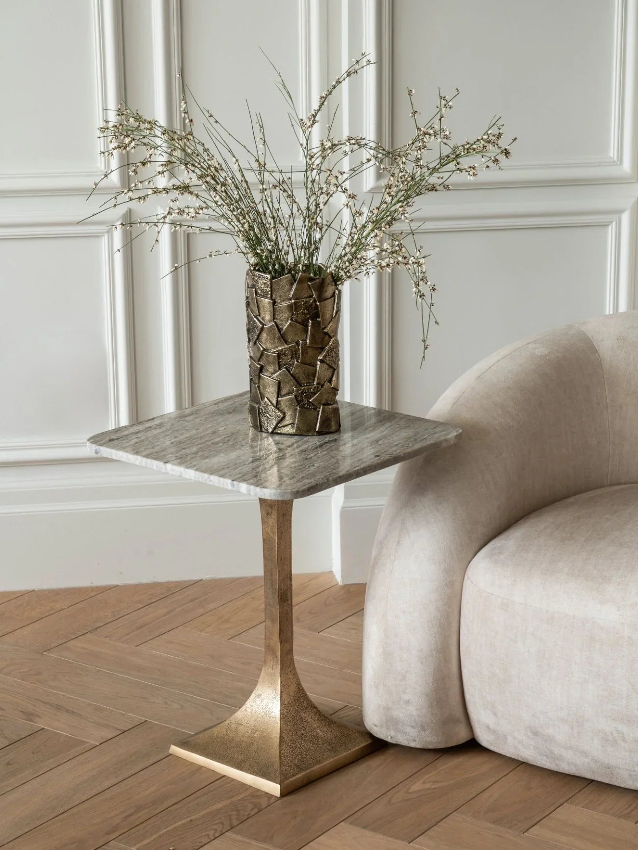 Marble side table with gold base beside cream sofa in elegant room.
