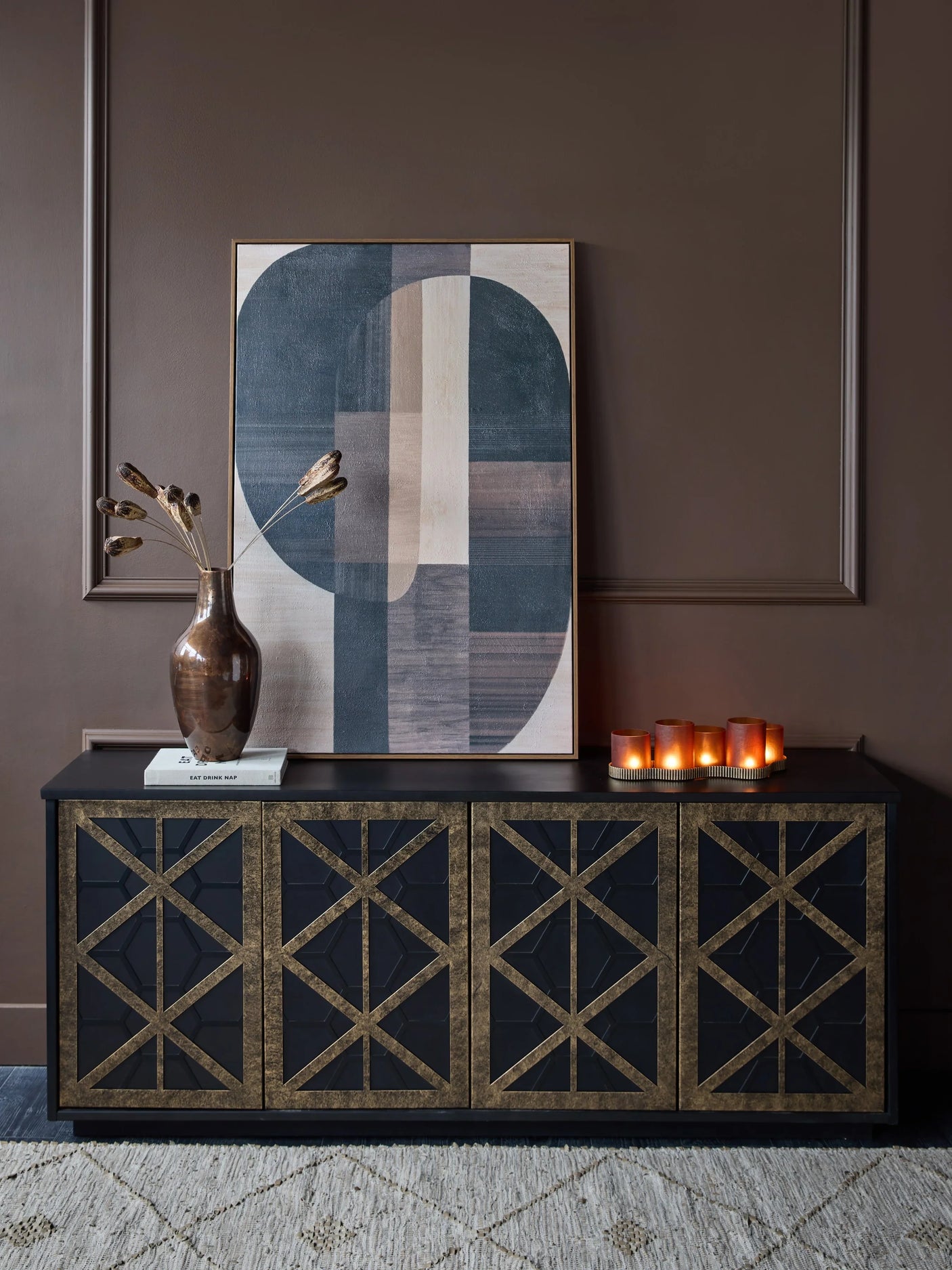 Black and gold sideboard in a brown room with abstract art and candles.