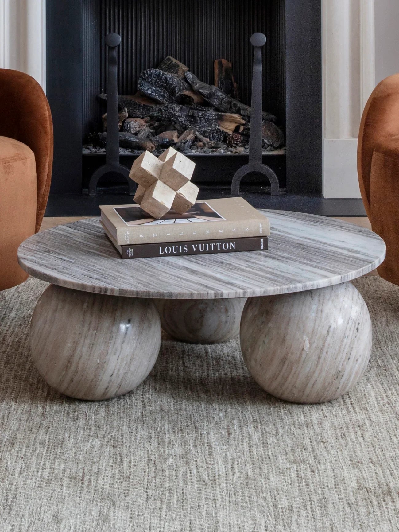Round marble coffee table with spherical legs in front of a fireplace.