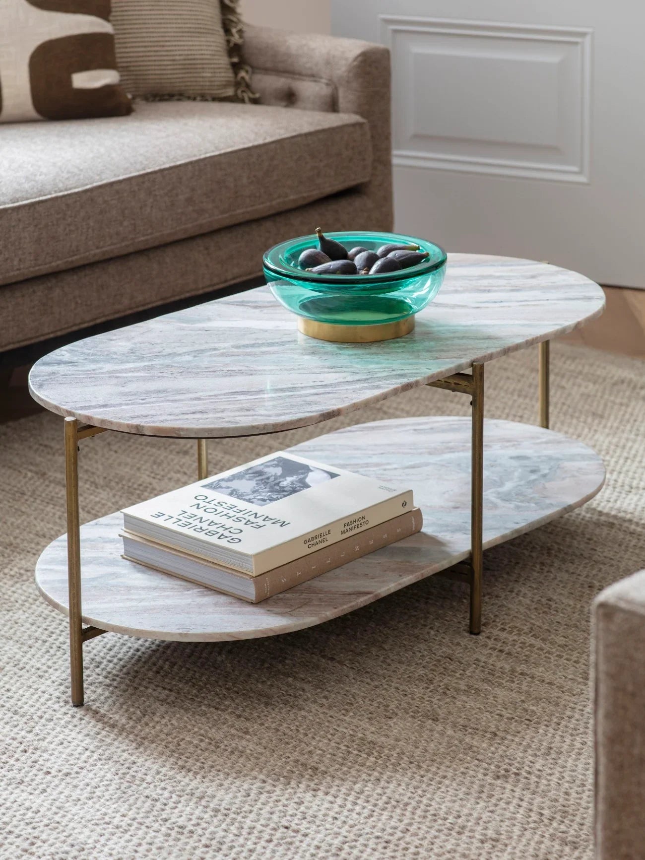 Oval marble coffee table with green bowl and books in cozy living room.