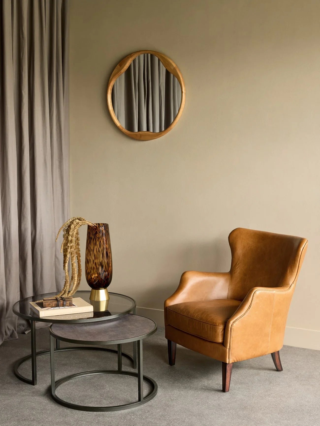 Nesting tables with glass and wood tops beside tan leather chair in cozy room.