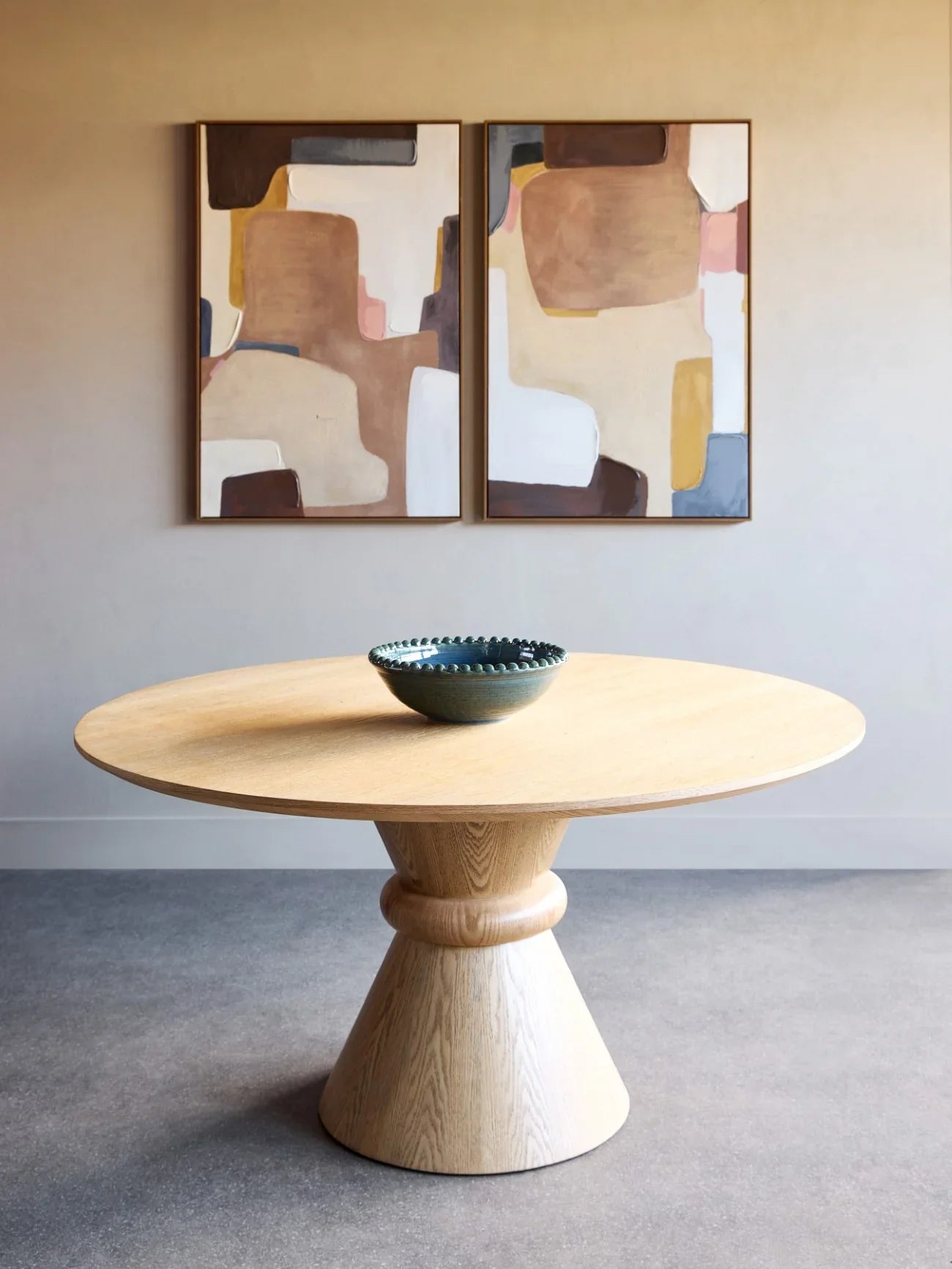 Round wooden dining table with pedestal base in modern room setting.