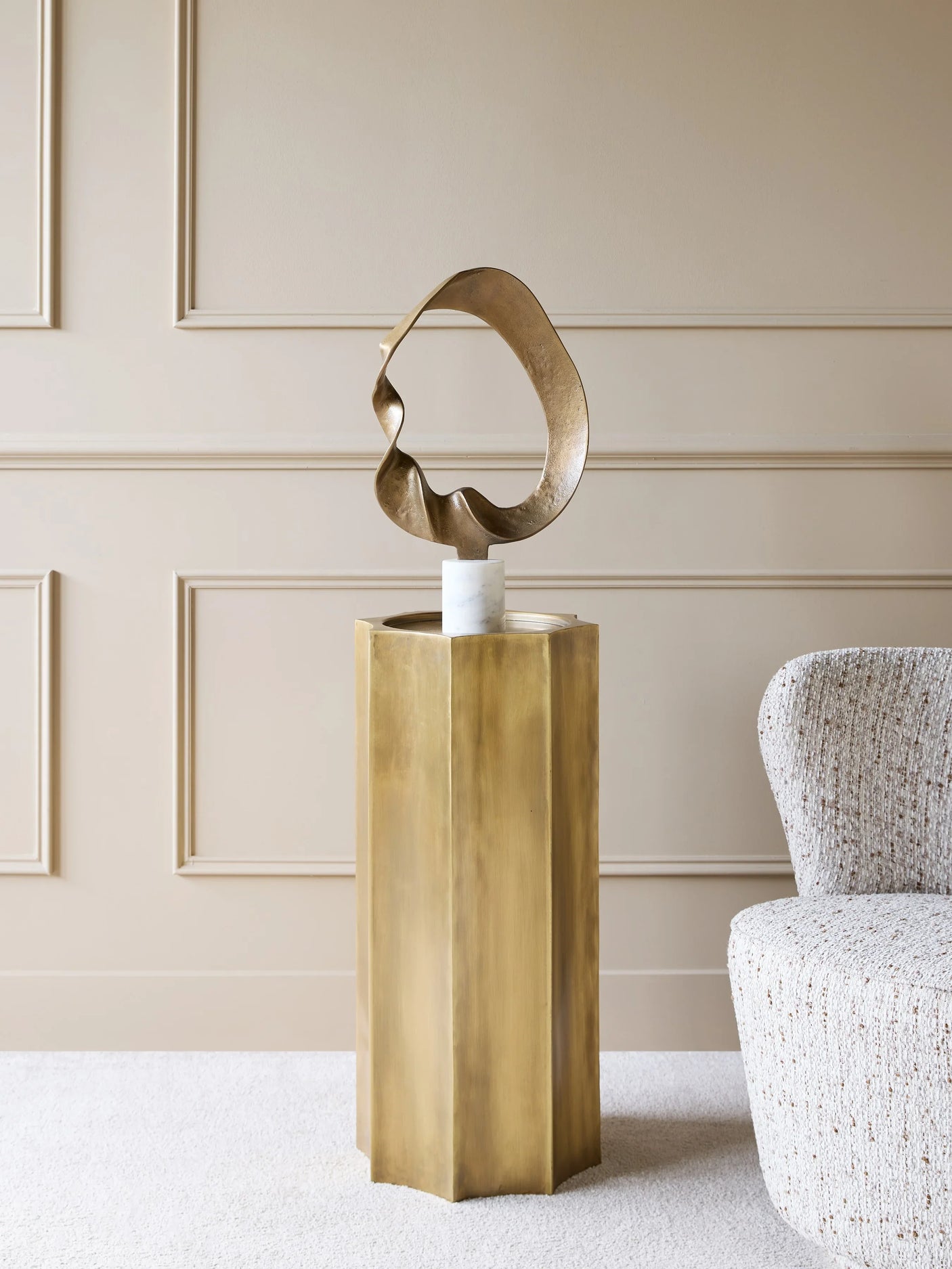 Antique brass pedestal with abstract sculpture in elegant living room setting.