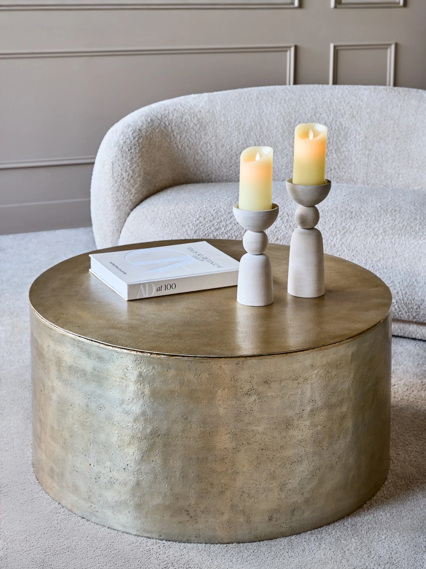 Gold metal drum coffee table with candles and book in cozy living room.