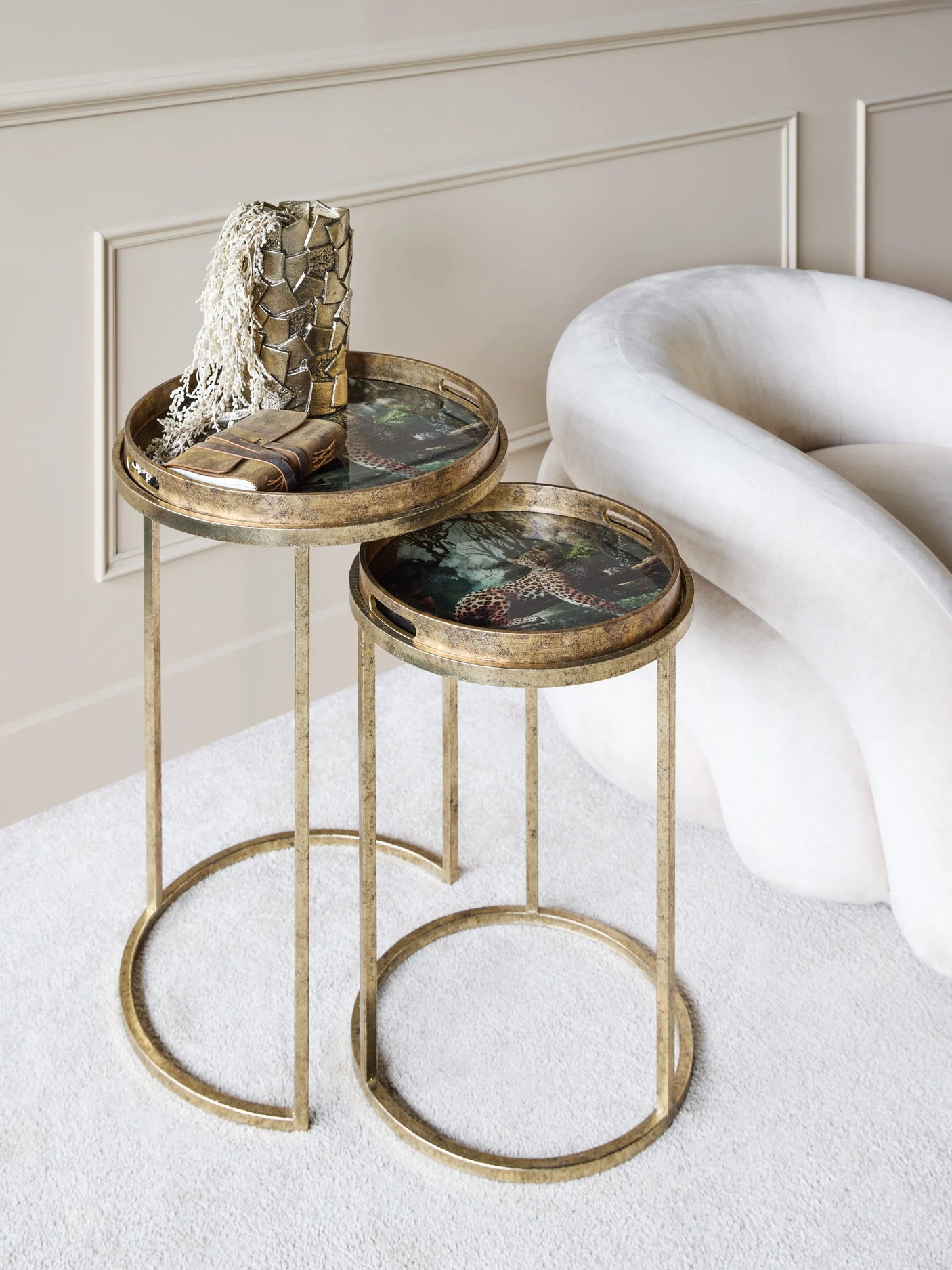 Gold side tables with leopard print tops beside a plush white chair.