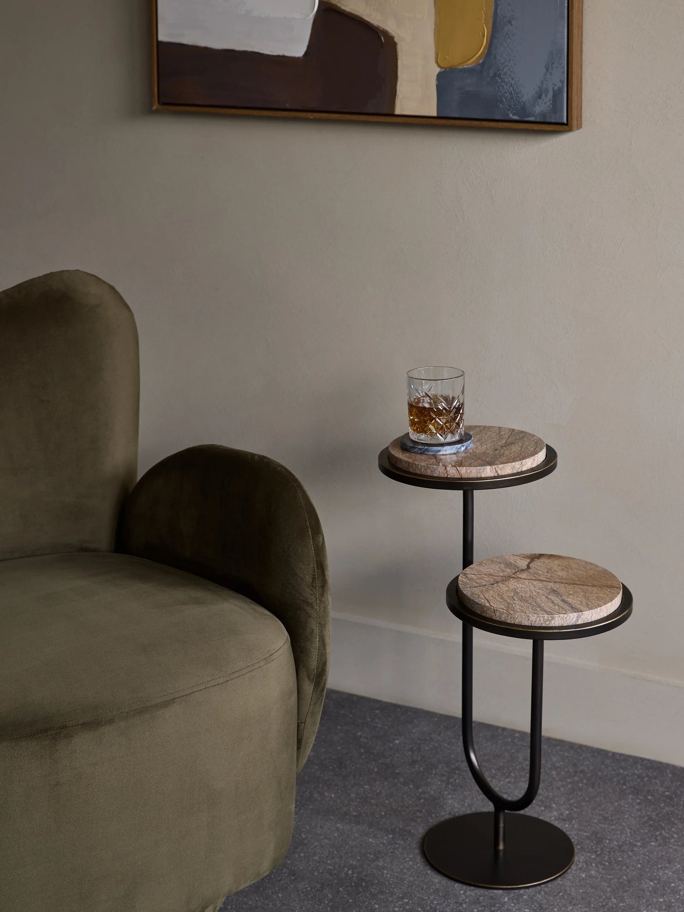 Two-tiered brown accent table beside a green velvet chair.