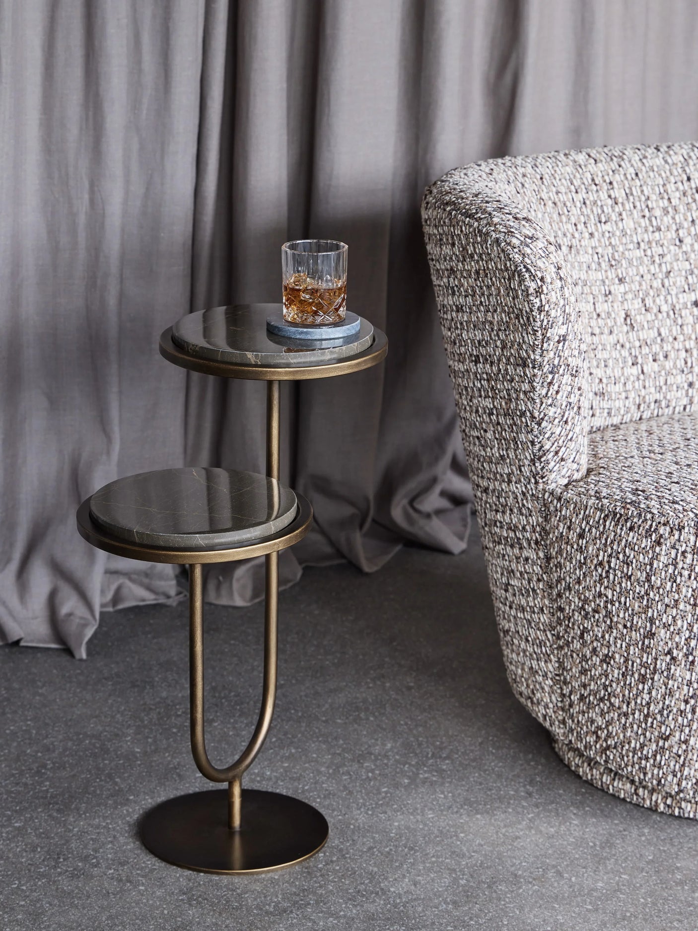 Gold marble accent table with a drink, next to a textured armchair.