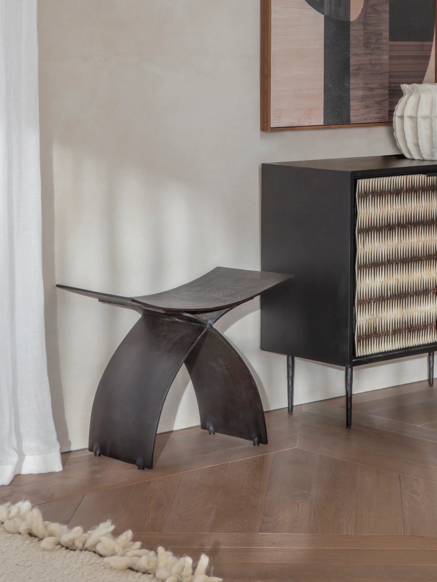 Dark iron stool in a modern room with wooden flooring and abstract artwork.