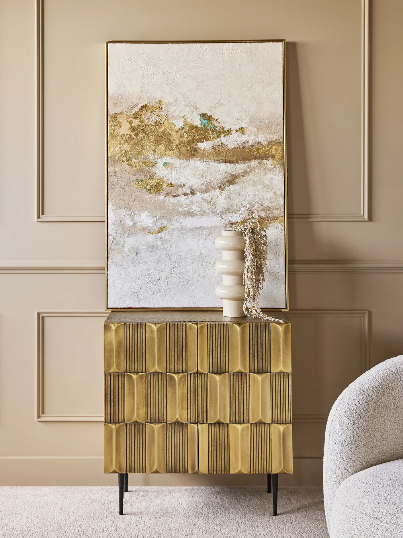 Gold-toned cabinet in elegant room with abstract art and vase.