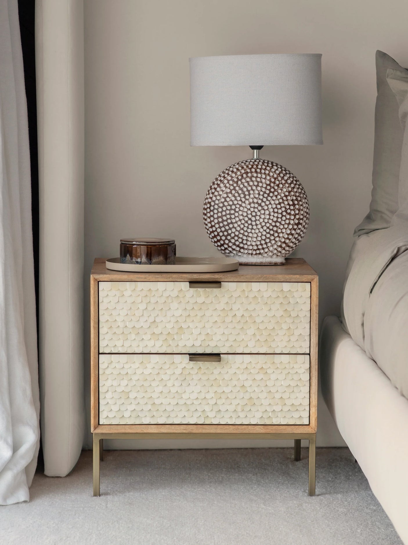 Cream inlay bedside table with textured drawers beside bed and lamp.