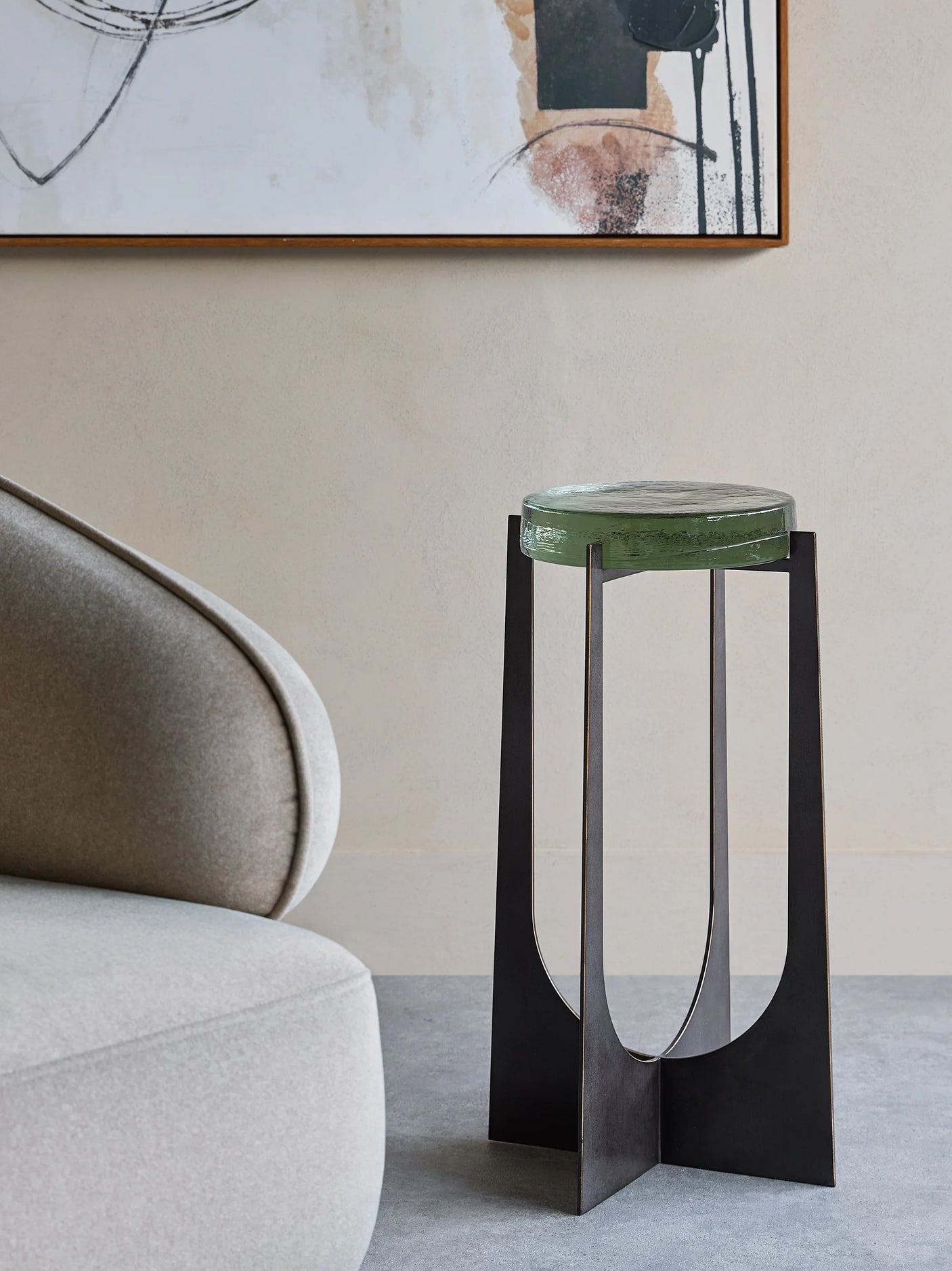 Green glass-topped accent table beside a modern beige chair in a stylish room.