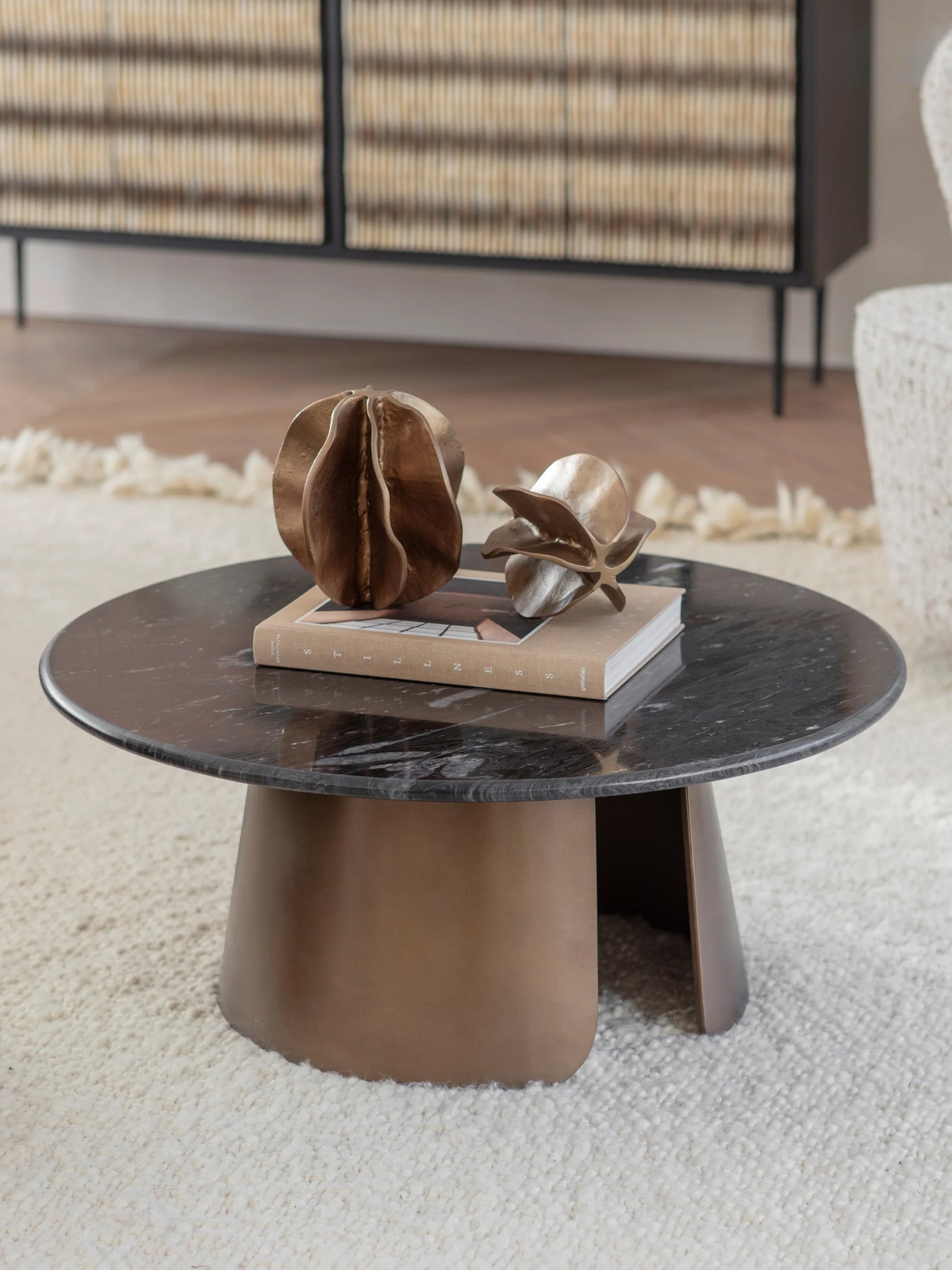 Round marble coffee table with bronze base, styled with decorative sculptures.
