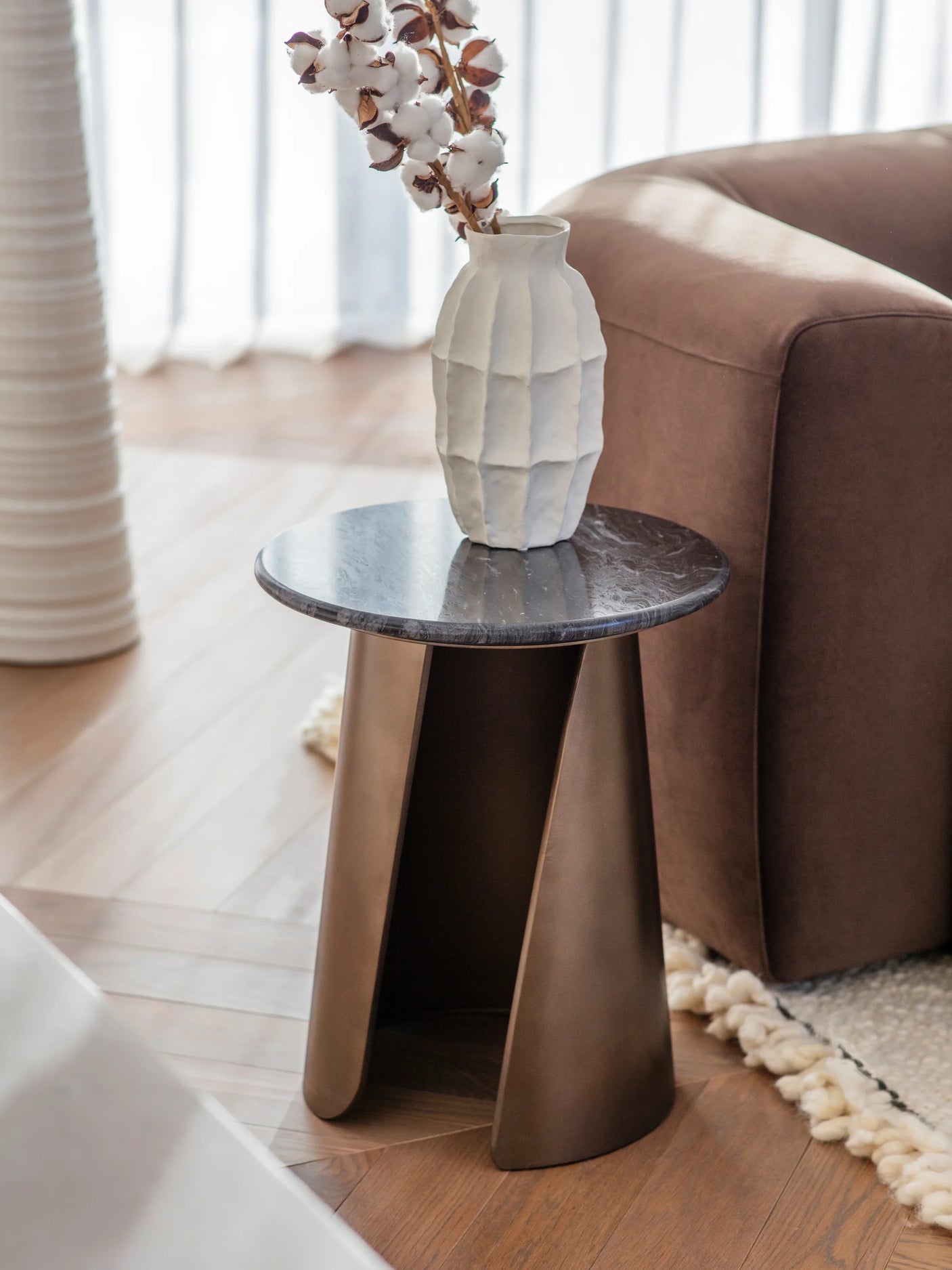 Bronze side table with marble top beside a brown sofa and white vase.