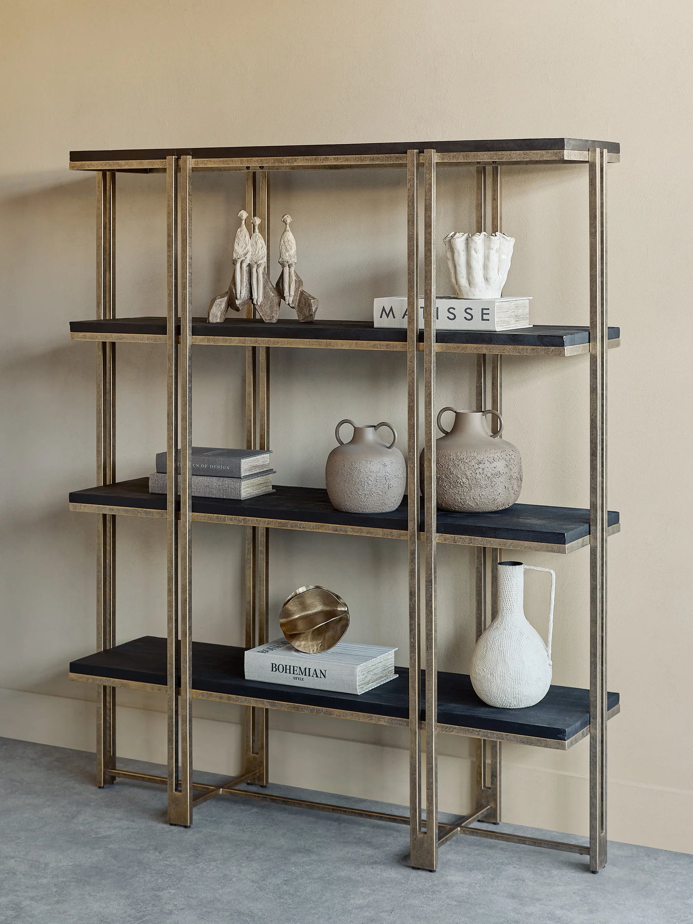 Gold-framed shelving with dark wood shelves, decorated with books and pottery.