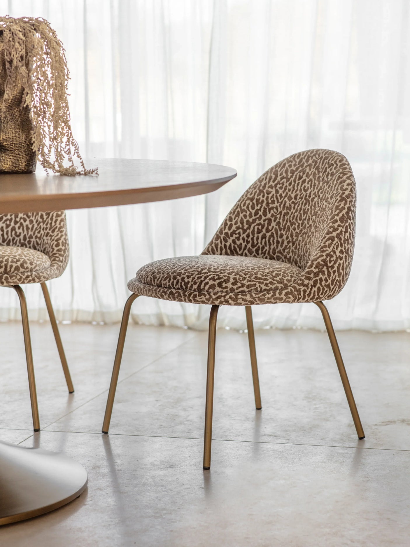 Leopard-patterned dining chair with gold legs beside a round table.