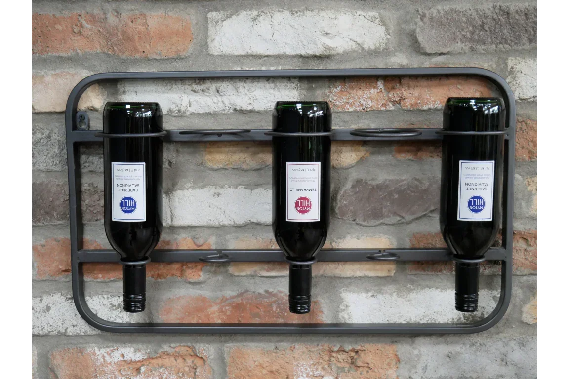 Wall-mounted metal wine rack holding three wine bottles against brick wall