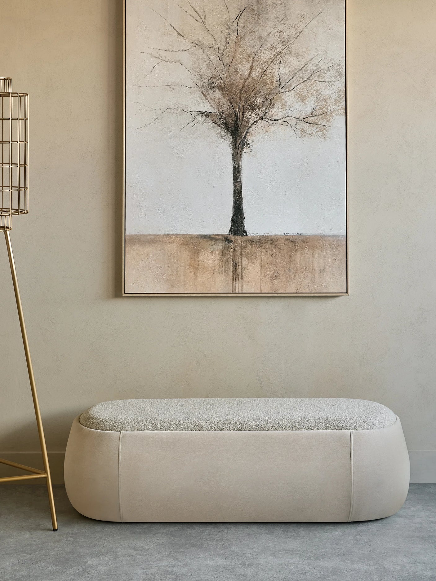 Beige upholstered bench beneath abstract tree painting in a minimalist room.