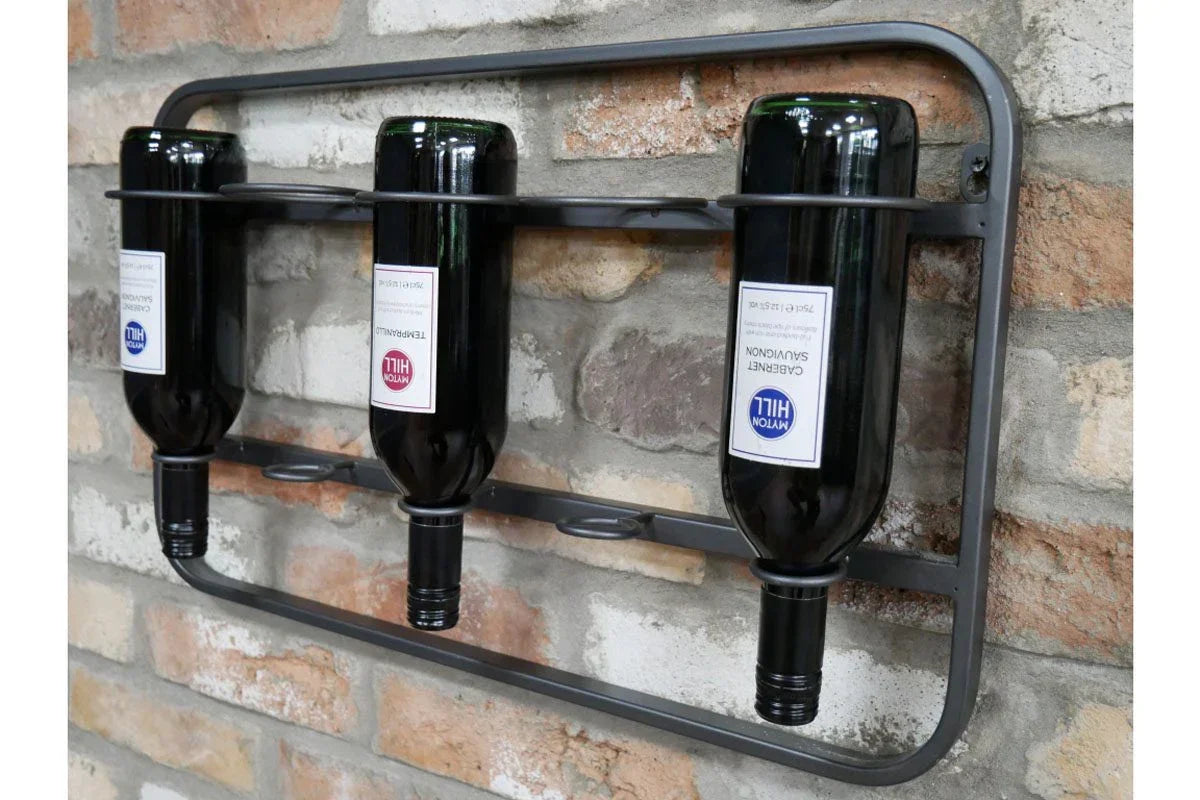 Wall-mounted metal wine rack holding three wine bottles against a brick wall
