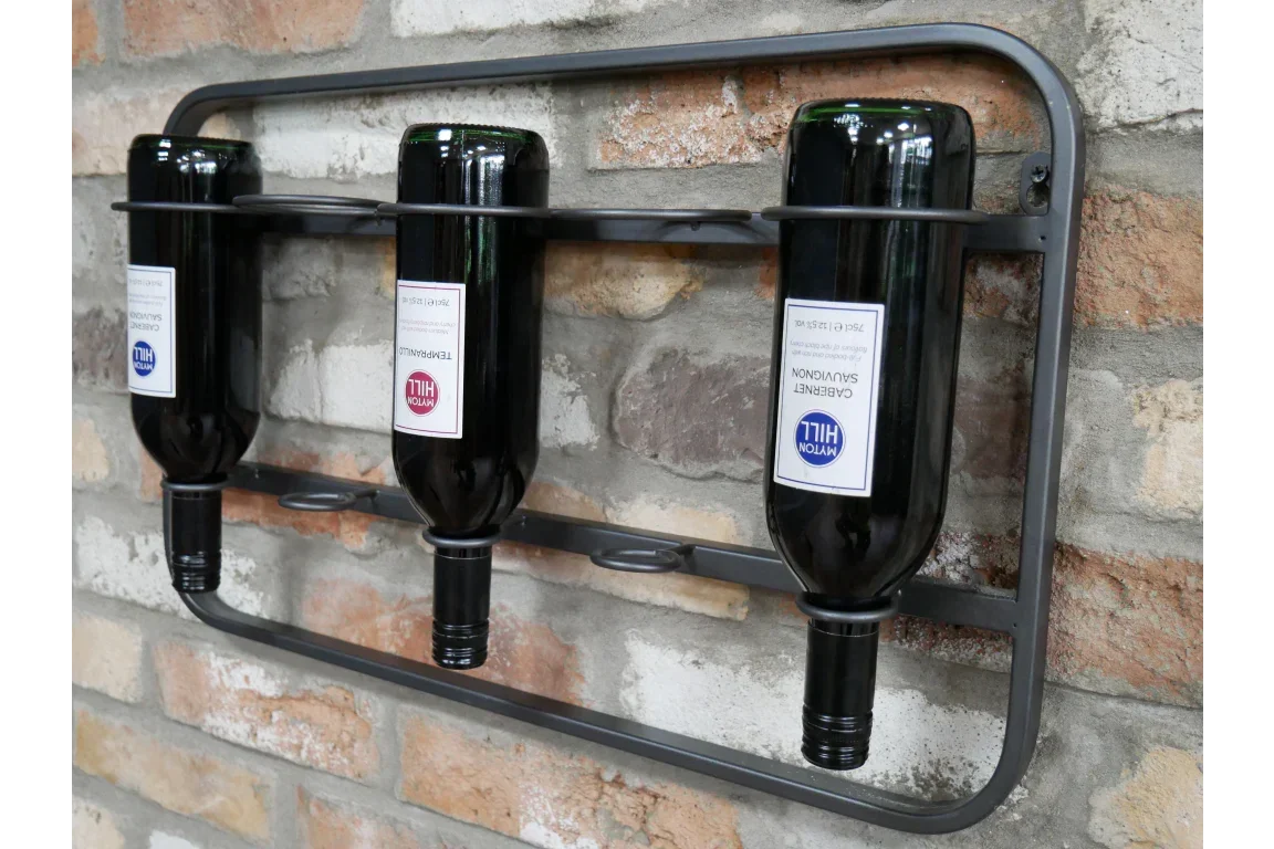 Wall mounted metal wine rack holding three bottles against exposed brick background