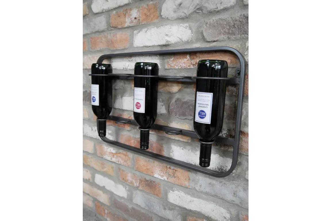 Metal wall mounted wine rack holding three wine bottles against a brick wall