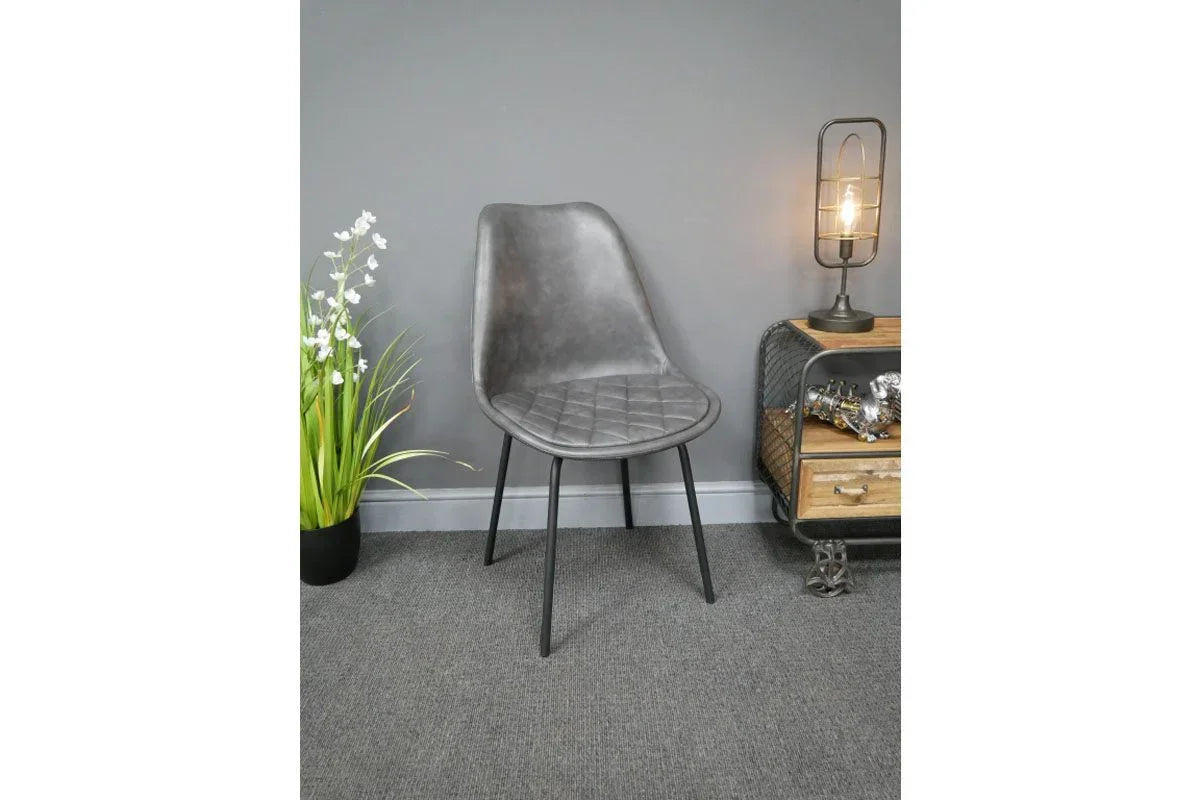 Grey faux leather dining chair with quilted seat and black metal legs against grey wall
