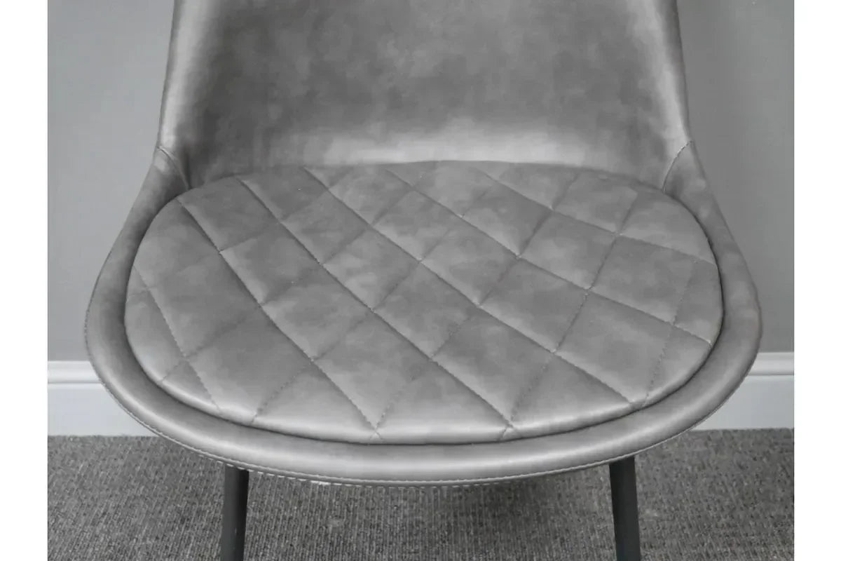 Grey quilted dining chair seat with padded faux leather and metal legs closeup
