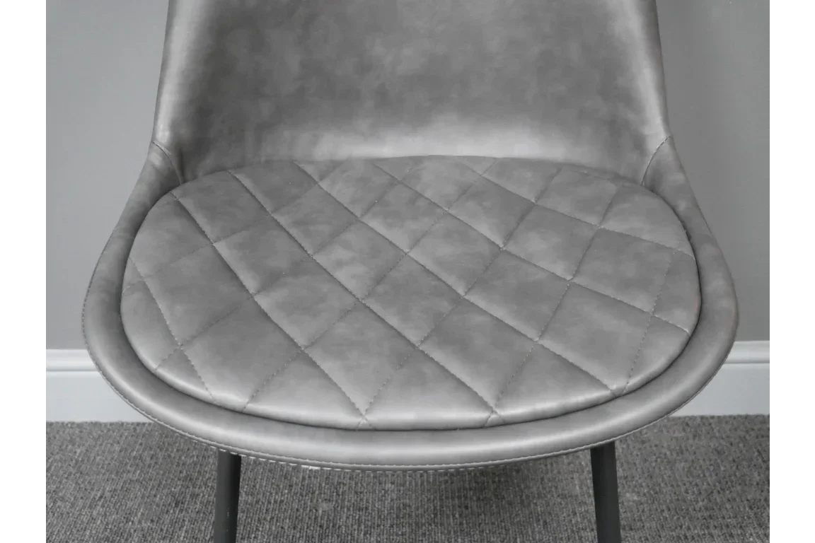 Grey faux leather dining chair with quilted seat and curved backrest on carpeted floor