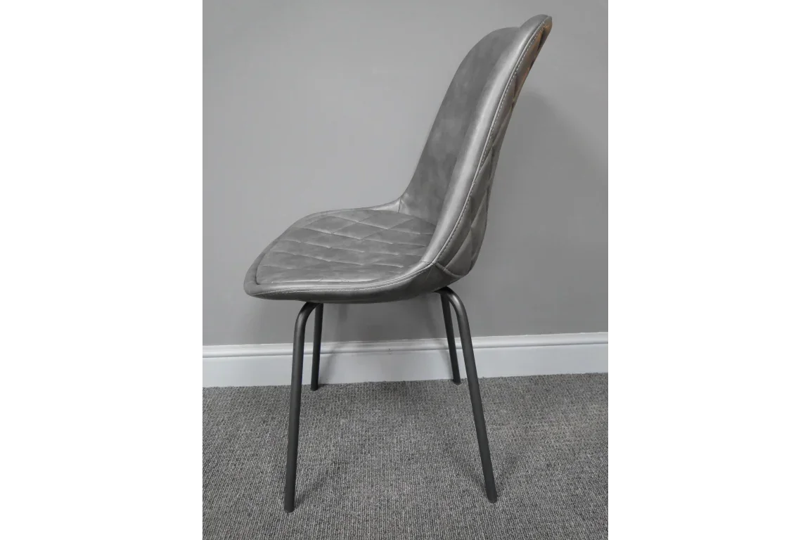 Grey dining chair with quilted seat and black metal legs, side view against grey wall