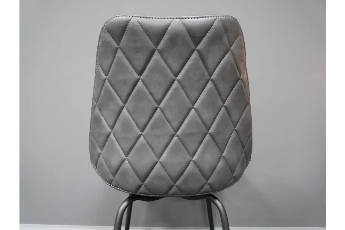 Grey dining chair with diamond quilted backrest and black metal legs against light wall