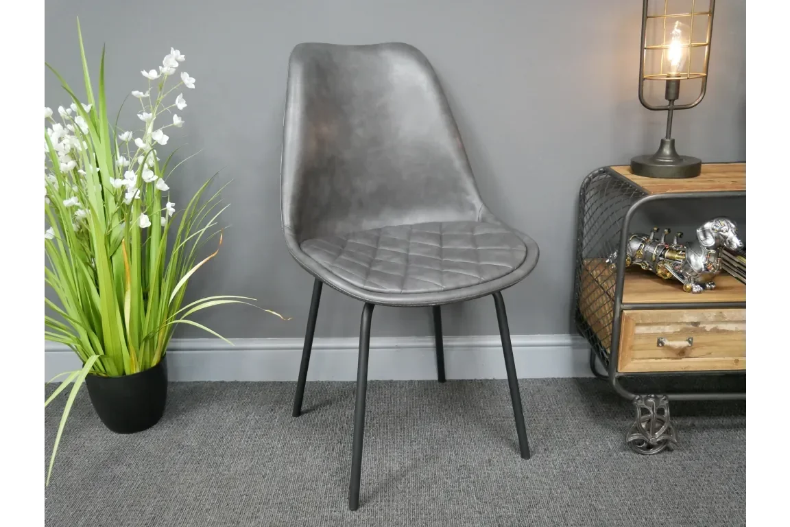 Grey dining chair with quilted seat and black legs beside plant and lamp
