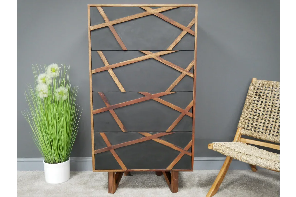 Tall black and wood chest of drawers with geometric front panel, beside plant and woven chair