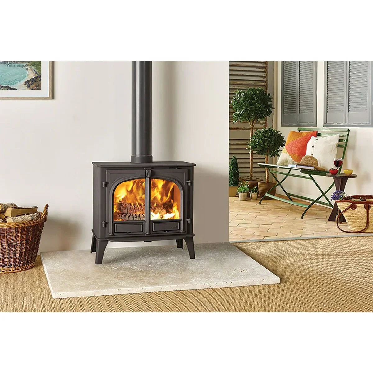 Black freestanding wood burning stove with fire, wicker log basket on hearth, modern interior