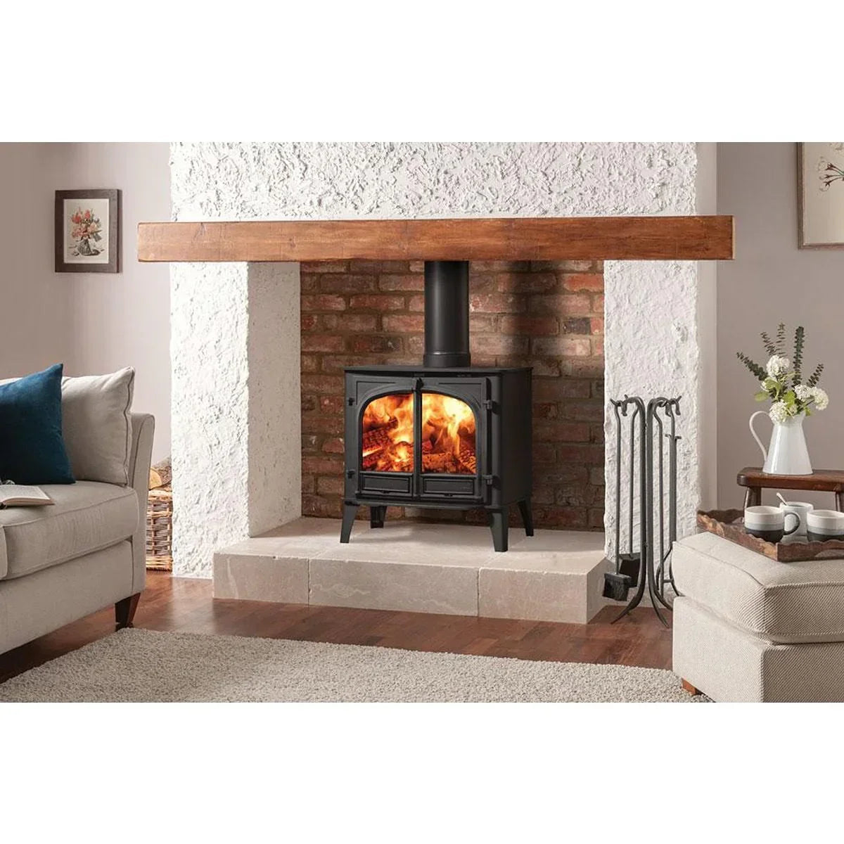 Black wood burning stove with glass doors and fire inside set in brick fireplace