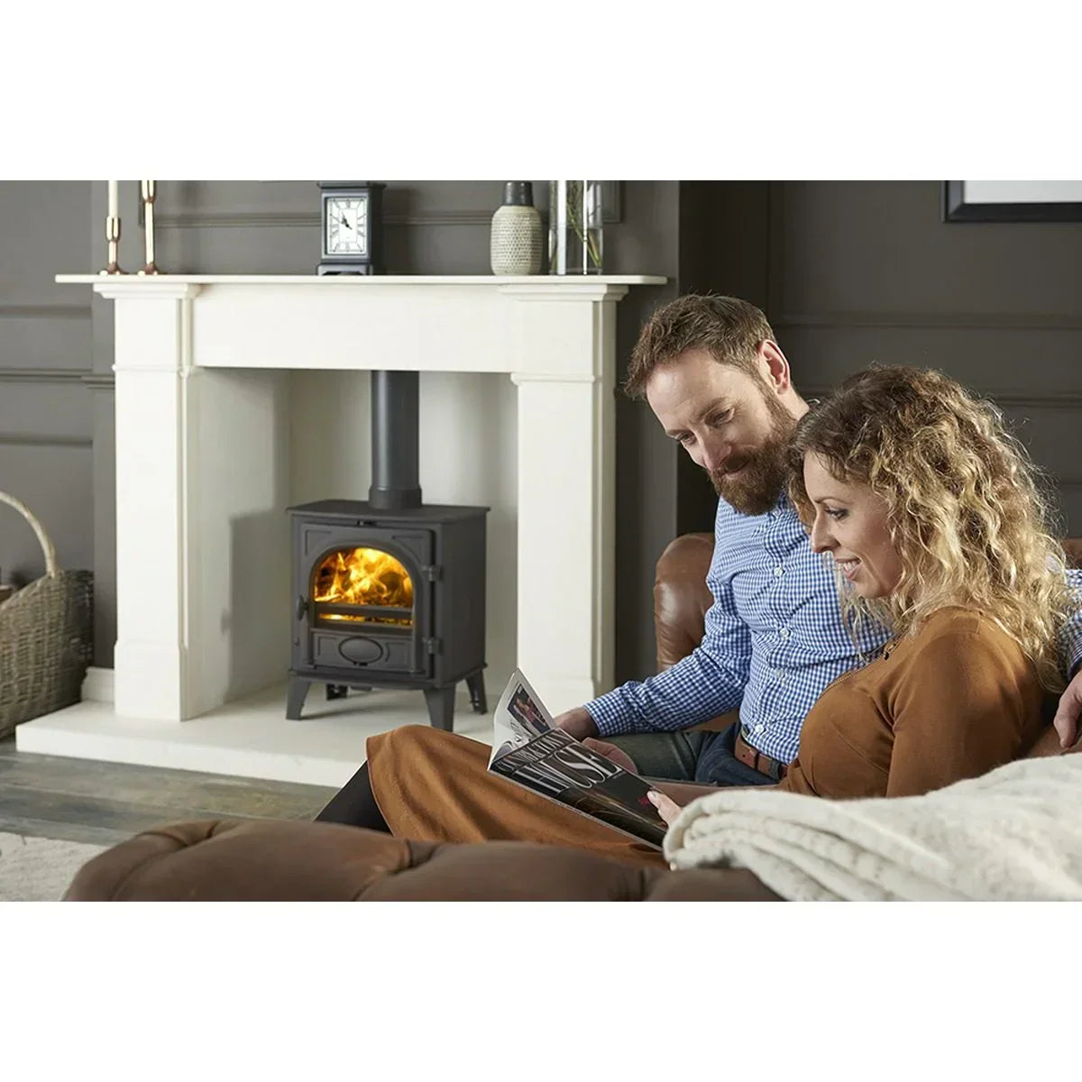 Living room with black wood burning stove, white fireplace surround, couple on brown sofa