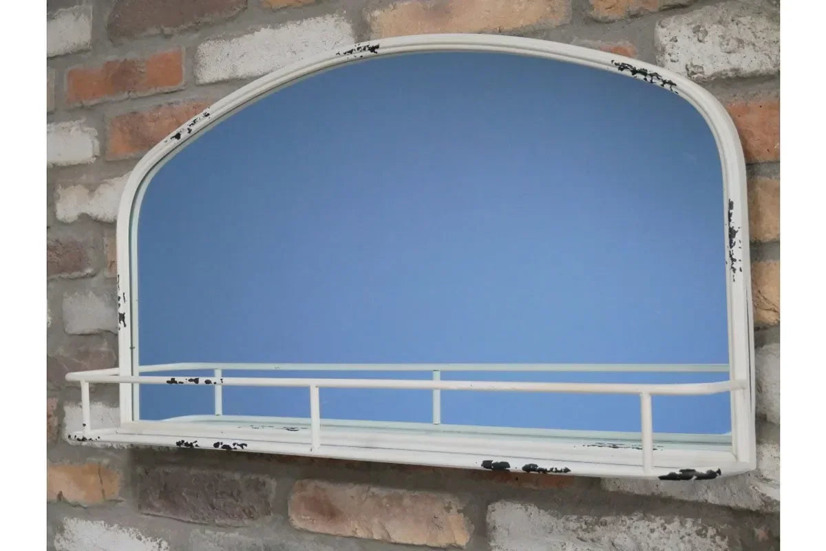 Arched wall mirror with distressed white metal frame and shelf against brick backdrop